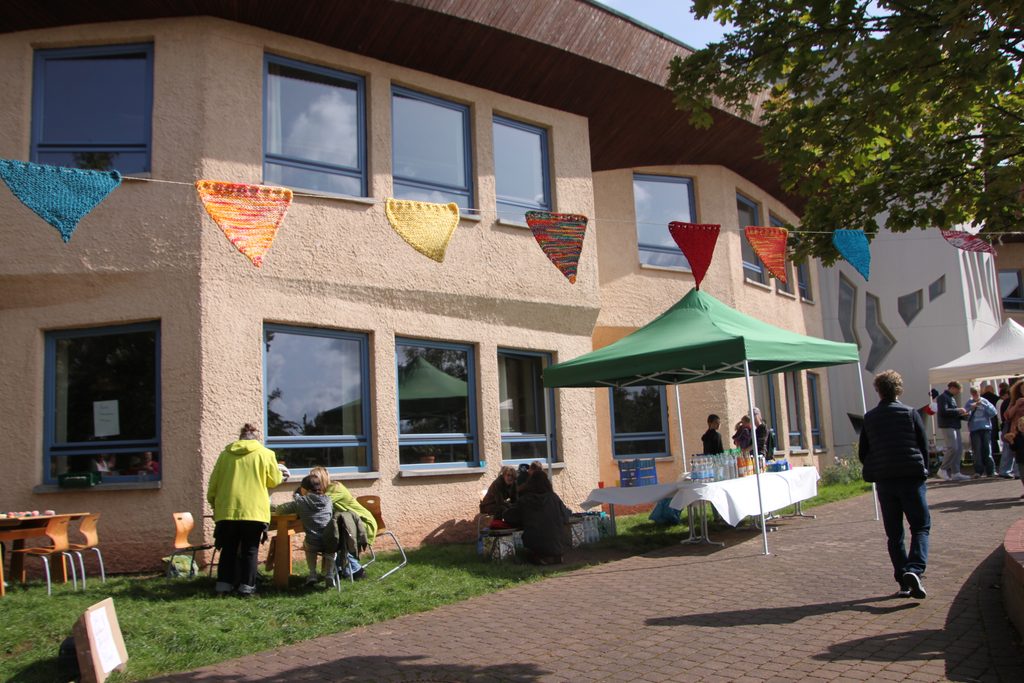 Das Schulgebäude aus der Aussenperspektive mit einer gehäkelten Wimpelgirlande bei einem Fest.